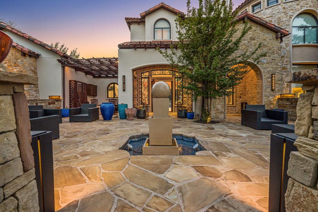 The private entry courtyard at dusk, a central stone fountain and iron-and-glass entry doors