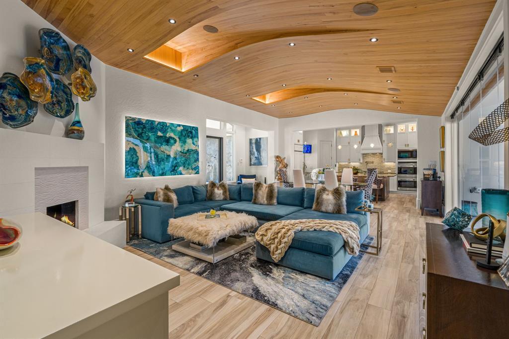 The family room with a curved wood-beamed ceiling, white porcelain-and-limestone fireplace, and sliding glass to the pool